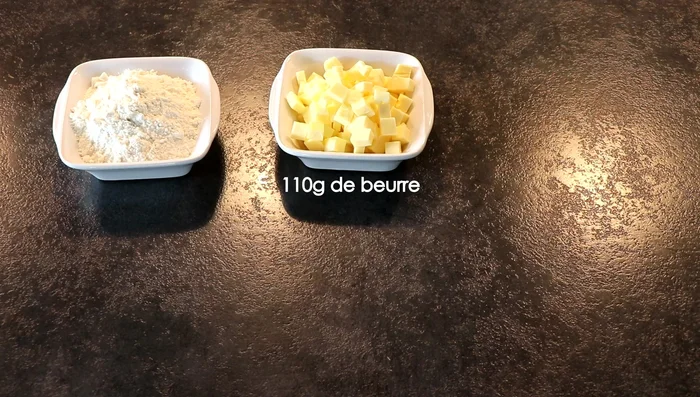 Préparation du biscuit sablé : Mélanger la farine, le sucre glace, la poudre d'amandes, la fleur de sel et la levure chimique. Ajouter le beurre coupé en dés et le rhum brun (ou extrait de vanille). Sabler la pâte du bout des doigts jusqu'à obtenir une boule homogène. Filmer et réfrigérer pendant au moins 1 heure.