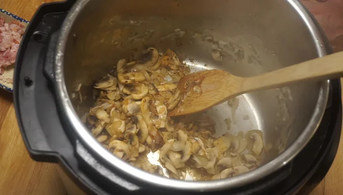 Dans l'Instant Pot, ajouter le lapin, les champignons, le mélange d'oignons et d'ail, le bouillon de poulet et le bacon.