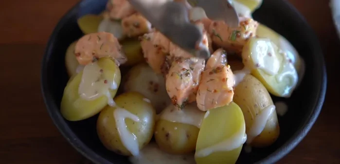 Ajouter le saumon cuit sur les pommes de terre, puis garnir d'oignons nouveaux et d'aneth.