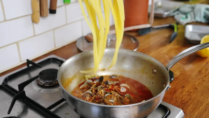 Ajouter les pâtes al dente à la sauce, ainsi que les palourdes, le jus de citron, le persil ciselé et un peu d'eau de cuisson des pâtes pour lier.