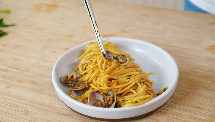 Dresser les pâtes en formant un tourbillon dans l'assiette, décorer avec des palourdes entières et un filet d'huile d'olive.