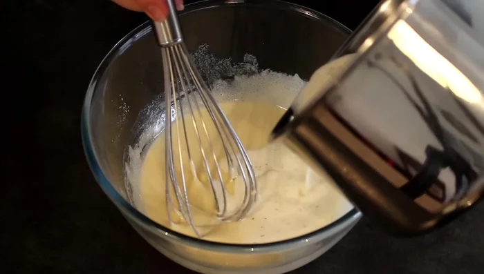 Retirer le lait du feu et la gousse de vanille. Verser le lait chaud petit à petit sur le mélange oeufs-sucre-farine en remuant.