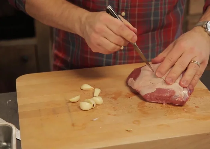 Piquer le gigot d'agneau avec des incisions et insérer des demi-gousses d'ail dans chaque incision.