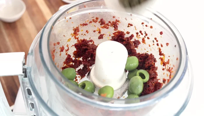 Ajouter les olives vertes, les câpres, l'ail pressé, le jus de citron, la moutarde, l'huile d'olive, le sel et le poivre au robot culinaire (ou dans un bol si vous travaillez à la main).