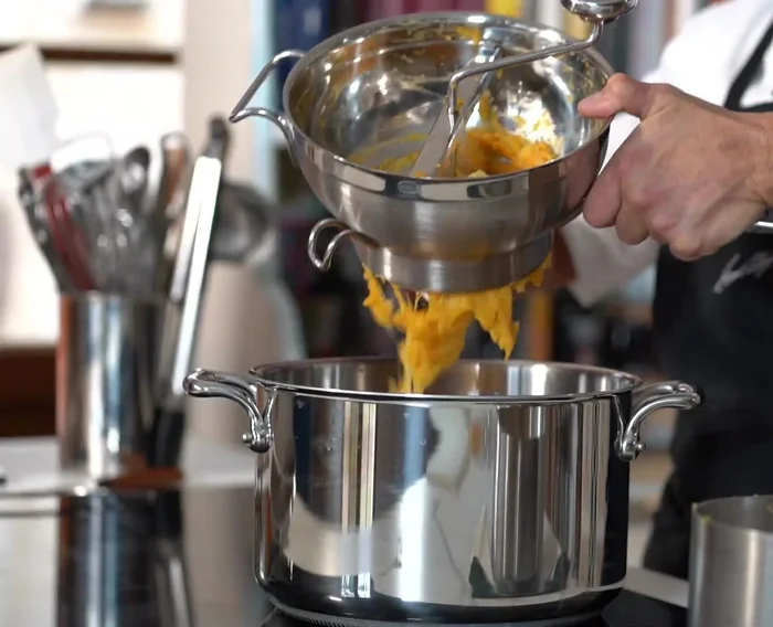 Préparation du gratin butternut-pommes de terre : cuire les légumes à l'eau, les passer au presse-purée, les faire sécher sur le gaz, ajouter beurre, parmesan, mascarpone.