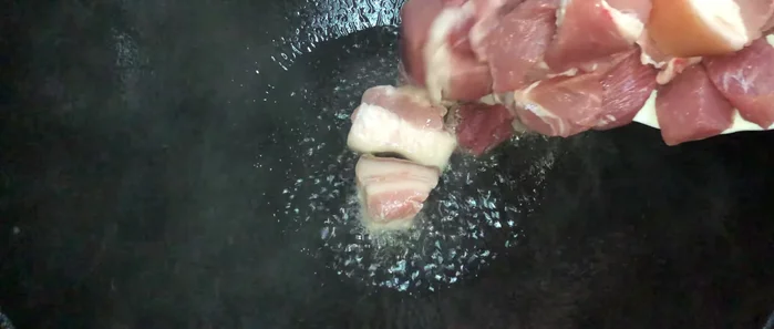 Ajouter les morceaux de porc dans la marmite chaude. Faire revenir la viande.
