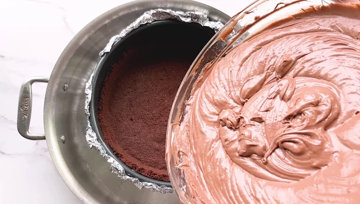Verser la pâte à cheesecake sur la croûte cuite. Placer le moule dans un bain-marie (le moule plus grand contenant de l'eau bouillante) et cuire au four pendant une heure.