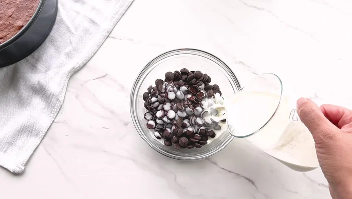 Préparer la ganache au chocolat en faisant fondre les pépites de chocolat noir avec de la crème chaude et de l'extrait de vanille (ou cognac/brandy). Fouetter jusqu'à consistance lisse et brillante. Verser sur le cheesecake refroidi.