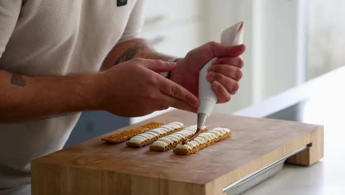 Montage du millefeuille : Placer les feuilles de pâte feuilletée. Pocher la ganache montée, la ganache au caramel, et le gel de mangue. Terminer avec les cacahuètes caramélisées.