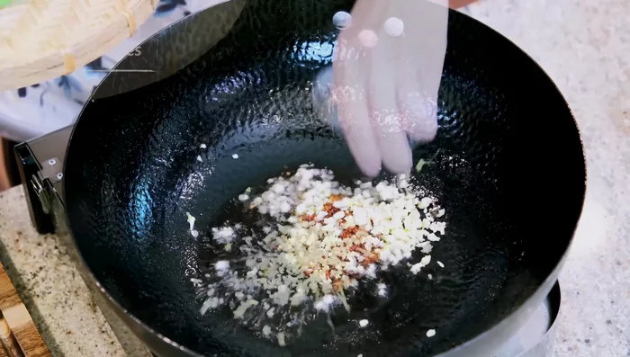 Faire sauter : Dans la même marmite (après avoir retiré la majeure partie de l'huile), faire sauter l'ail, le gingembre, les flocons de piment et la partie blanche des oignons verts jusqu'à ce que le parfum se dégage.