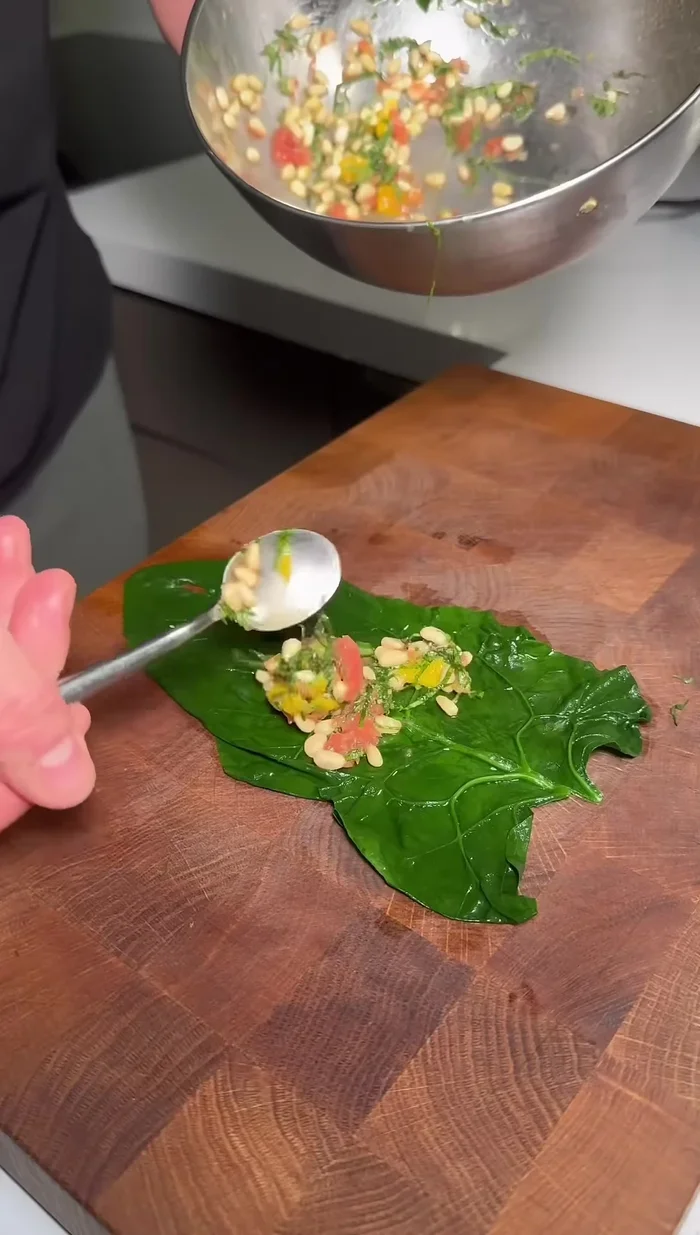 Monter l'entrée: déposer une feuille d'épinard, puis une escalope de foie gras, côté le plus bas vers le haut, et ajouter la farce.