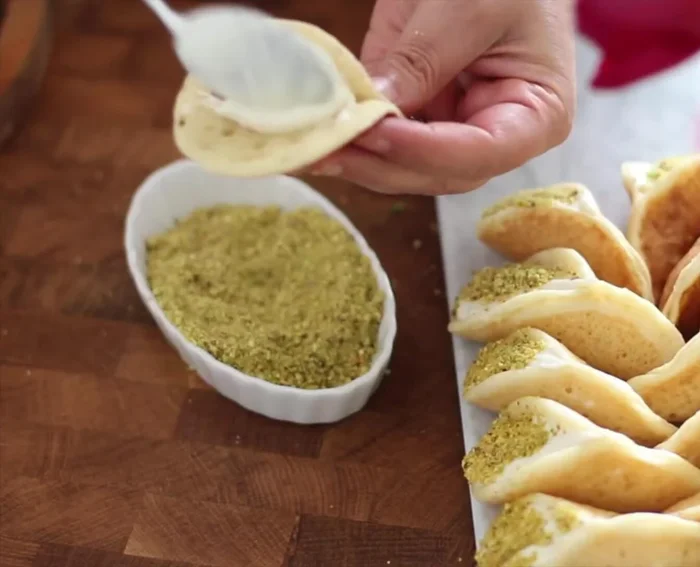 Montage des KATF : Déposer une cuillère à soupe de crème sur une crêpe, plier et pincer les extrémités aux deux tiers pour lui donner une forme courbée. Saupoudrer de pistaches.