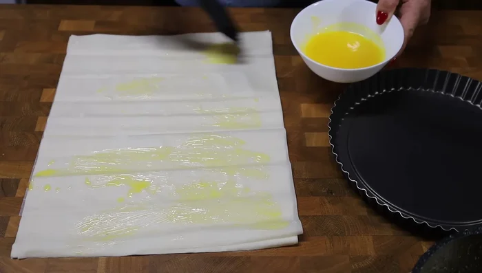 Badigeonner les feuilles de pâte filo de beurre fondu ou de margarine, puis les superposer dans le moule en les laissant dépasser légèrement sur les bords. Travailler rapidement car la pâte sèche vite.