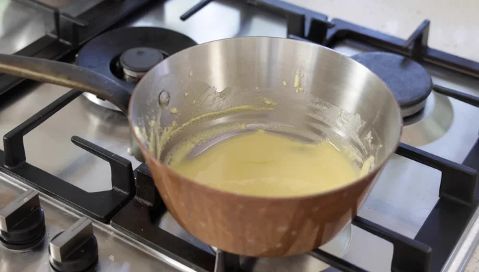 Assemblage de la béchamel : Tamiser le roux refroidi dans le lait aromatisé chaud. Bien mélanger au fouet pour éviter les grumeaux. Ajouter le reste du lait, remettre sur feu moyen et laisser mijoter pendant 3 minutes en remuant.
