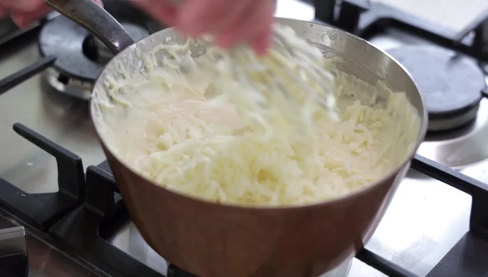 Incorporer la Garniture : Ajouter le fromage râpé, le jambon Serrano coupé et le persil haché à la béchamel. Mélanger délicatement. (438.4)