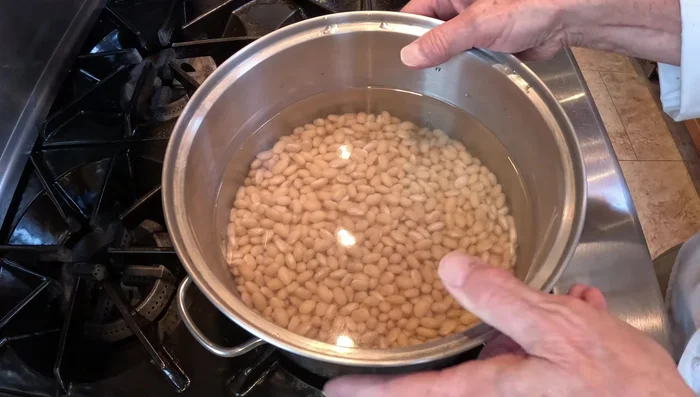 Faire tremper les haricots secs toute la nuit. Les cuire à feu moyen avec du bouillon de poulet, du concentré de tomates, des oignons, de l'ail et un bouquet garni pendant 45 minutes à 1 heure, jusqu'à ce qu'ils soient tendres.