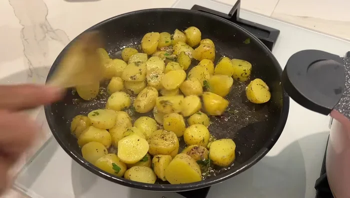 Préparation des pommes de terre sautées : Laver les pommes de terre (peau optionnelle), ajouter de l'huile d'olive, sel, poivre, ail, persil et coriandre. Faire revenir jusqu'à ce qu'elles soient dorées.