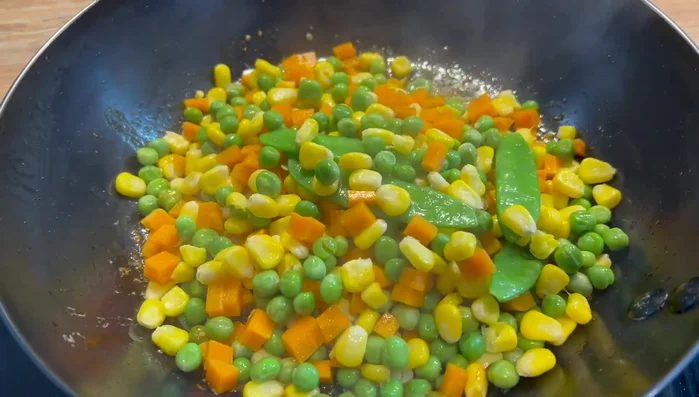 Une fois les têtes retirées, ajouter les légumes à la poêle, suivis des morceaux de crevettes.