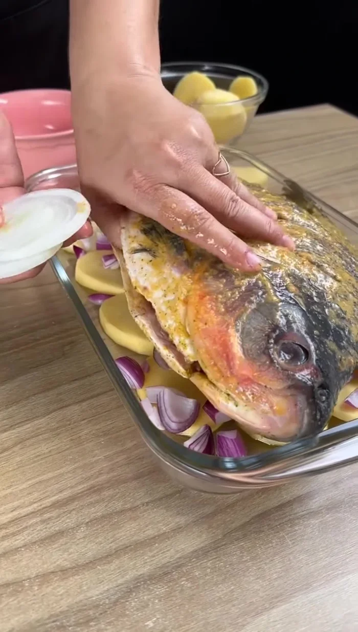 Déposer le poisson sur les légumes. Ajouter des rondelles d'oignons, de poivrons rouges et jaunes, et de la coriandre ou du persil haché finement à l'intérieur du poisson.