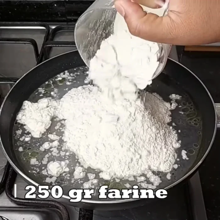 Verser progressivement la farine dans l'eau bouillante tout en remuant énergiquement. (Il est possible d'ajouter un peu d'huile d'olive pour éviter que la pâte ne colle).