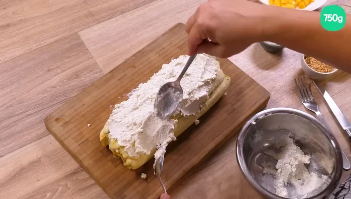 Tartiner la bûche avec le reste de la crème au yaourt. Décorer avec le pralin, les dés de kiwi et de mangue restants, des graines de grenade et des copeaux de noix de coco.