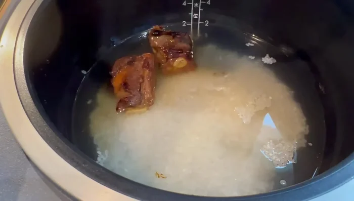 Dans un cuiseur à riz, ajouter le riz, l'eau, les morceaux de viande, le reste de la marinade et tous les légumes.