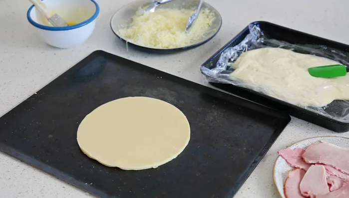 Montage du pithivier : Placer le plus grand disque de pâte sur une plaque de cuisson farinée (478.879). Étaler une couche de jambon (570.959), suivie de béchamel (575.12) et de fromage (578.32). Répéter l’opération pour une deuxième couche. Badigeonner le bord de la pâte avec de l’œuf battu (617.519).