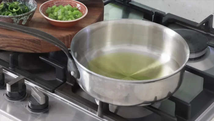 Préparer la garniture : Dans une poêle, faire chauffer l'huile d'olive. Ajouter l'ail, les piments verts (et poivrons si désiré), et les tomates. Laisser mijoter doucement pendant 5 minutes, jusqu'à obtenir une sorte de fondue.