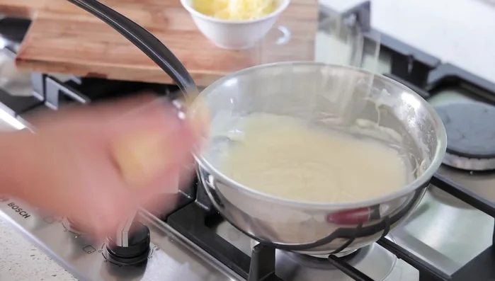 Hors du feu, ajouter le fromage râpé petit à petit à l'aide d'une cuillère, en mélangeant délicatement pour éviter les grumeaux.