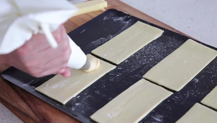 Déposer des copeaux de fromage sur la sauce. Placer un second rectangle de pâte feuilletée sur le dessus, en pressant légèrement les bords.