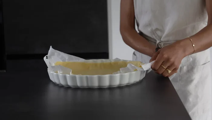 Préparer la pâte sablée (acheter du commerce ou faire maison). Piquer le fond avec une fourchette et le couvrir de papier cuisson. Ajouter un poids (haricots secs, riz...) pour éviter que la pâte ne gonfle.