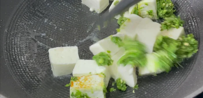 Ajouter la pâte d'ail, piments verts et coriandre au paneer. Bien mélanger et cuire jusqu'à ce que le paneer soit doré et que les arômes se mélangent.