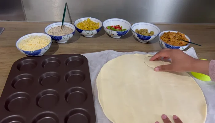 A l'aide d'un emporte-pièce, découper des ronds dans la pâte feuilletée et les disposer dans un moule à mini-tarts.