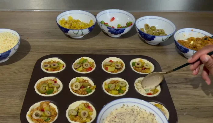 Ajouter une cuillère à soupe d'appareil à quiche dans chaque mini quiche, puis du fromage râpé et des herbes de Provence (ou de l'origan).