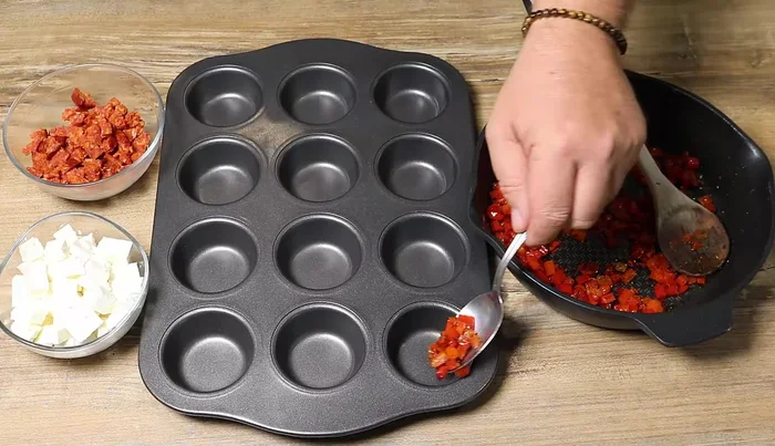Répartir un peu de poivron, de chorizo et de feta dans chaque cavité d'un moule à muffins.