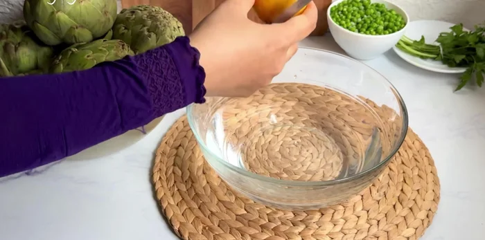 Pendant ce temps, préparer les artichauts: casser la tige, enlever les feuilles dures, couper le haut pointu et éplucher la base. Retirer le foin à l'intérieur. Les plonger dans de l'eau citronnée pour éviter qu'ils noircissent.